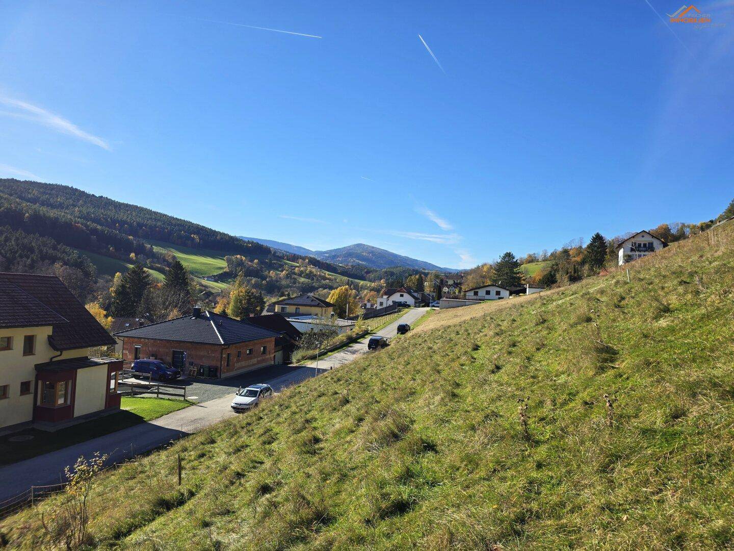 Panoramablick auf eine sanfte Hügellandschaft mit Häusern und weiten Feldern unter blauem Himmel.