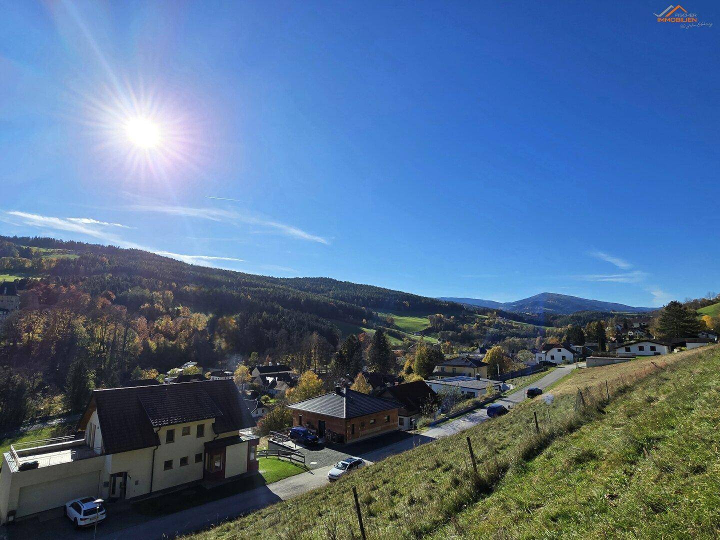 Weitläufiger Ausblick über eine grüne Hügellandschaft mit verstreuten Häusern unter strahlend blauem Himmel.