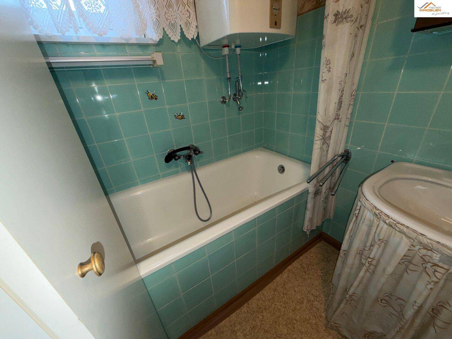 Badezimmer mit türkisfarbenen Fliesen, Badewanne und Boiler, im Stil der 80er Jahre.