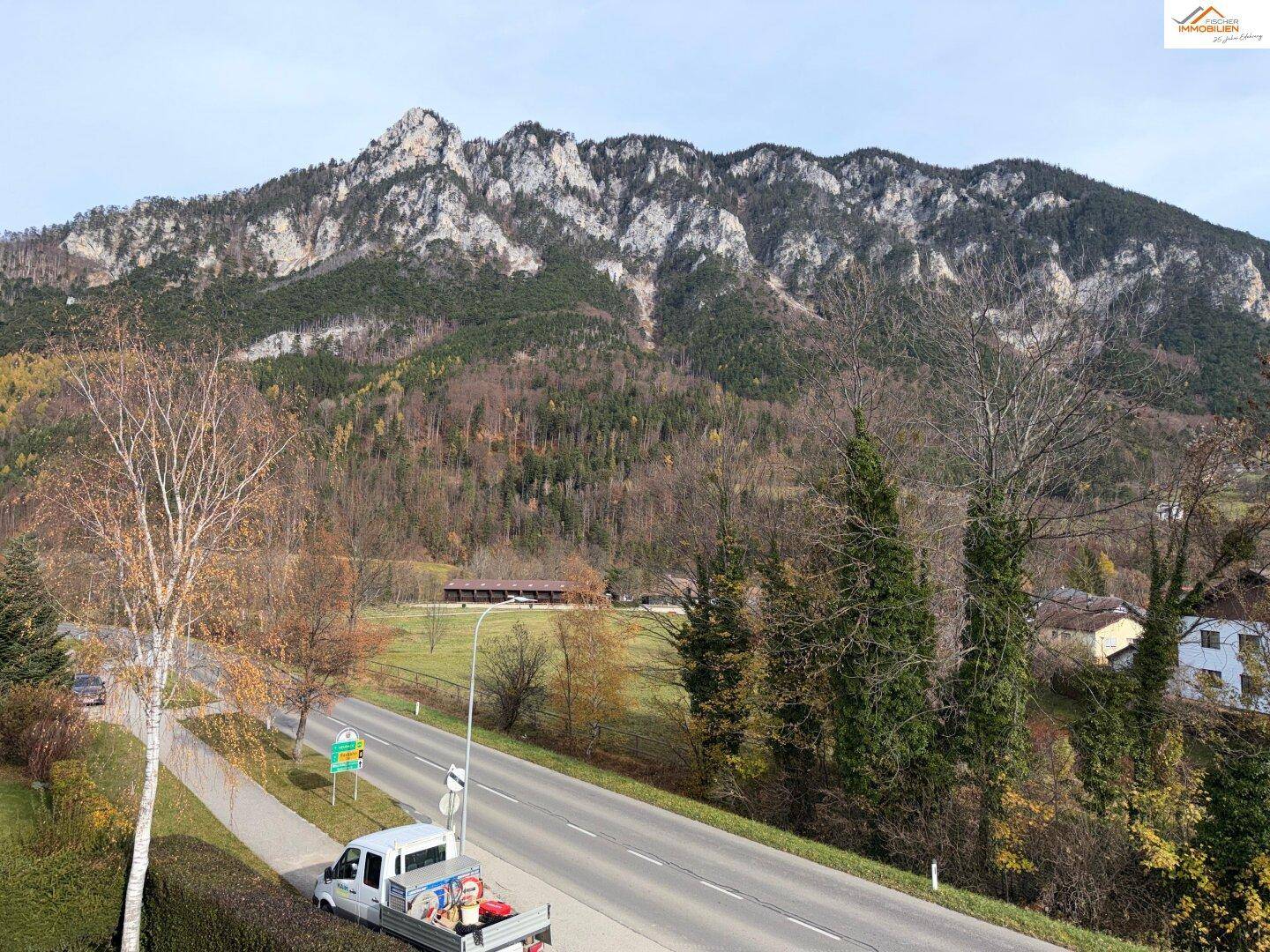 Weitläufiger Blick auf eine Straße, Bäume und die beeindruckende Berglandschaft.