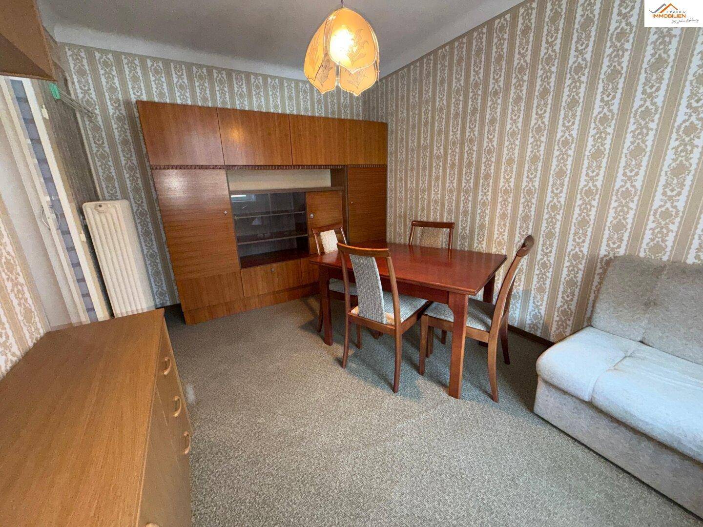 Essbereich mit Holztisch, Stühlen und einem großen Schrank, angrenzend an einen Wohnbereich.