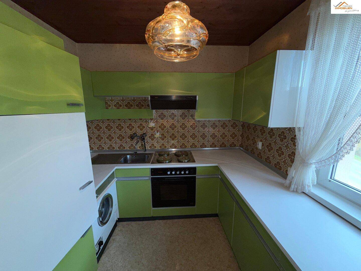 Grüne Küche im Retro-Stil mit gemusterten Fliesen und einem Fenster mit Vorhang.