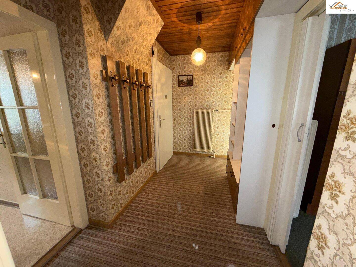 Langer Flur mit Holzdecke, gemusterter Tapete und Heizkörper, der viel Platz bietet.