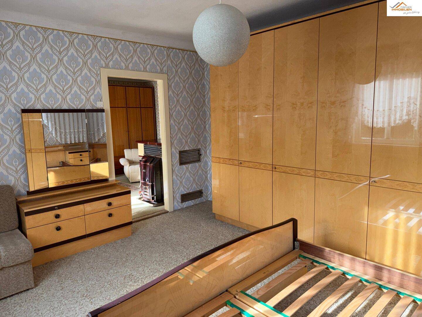 Geräumiges Schlafzimmer mit großem Kleiderschrank, Kommode und Zugang zu einem weiteren Raum.