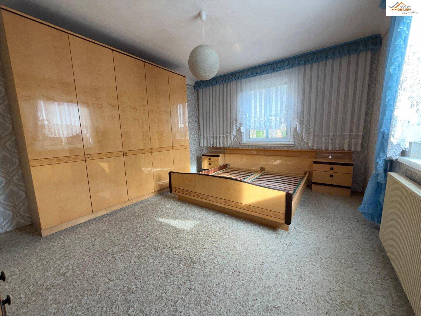 Schlafzimmer mit großem Kleiderschrank, Bett und Fenster mit Vorhängen.