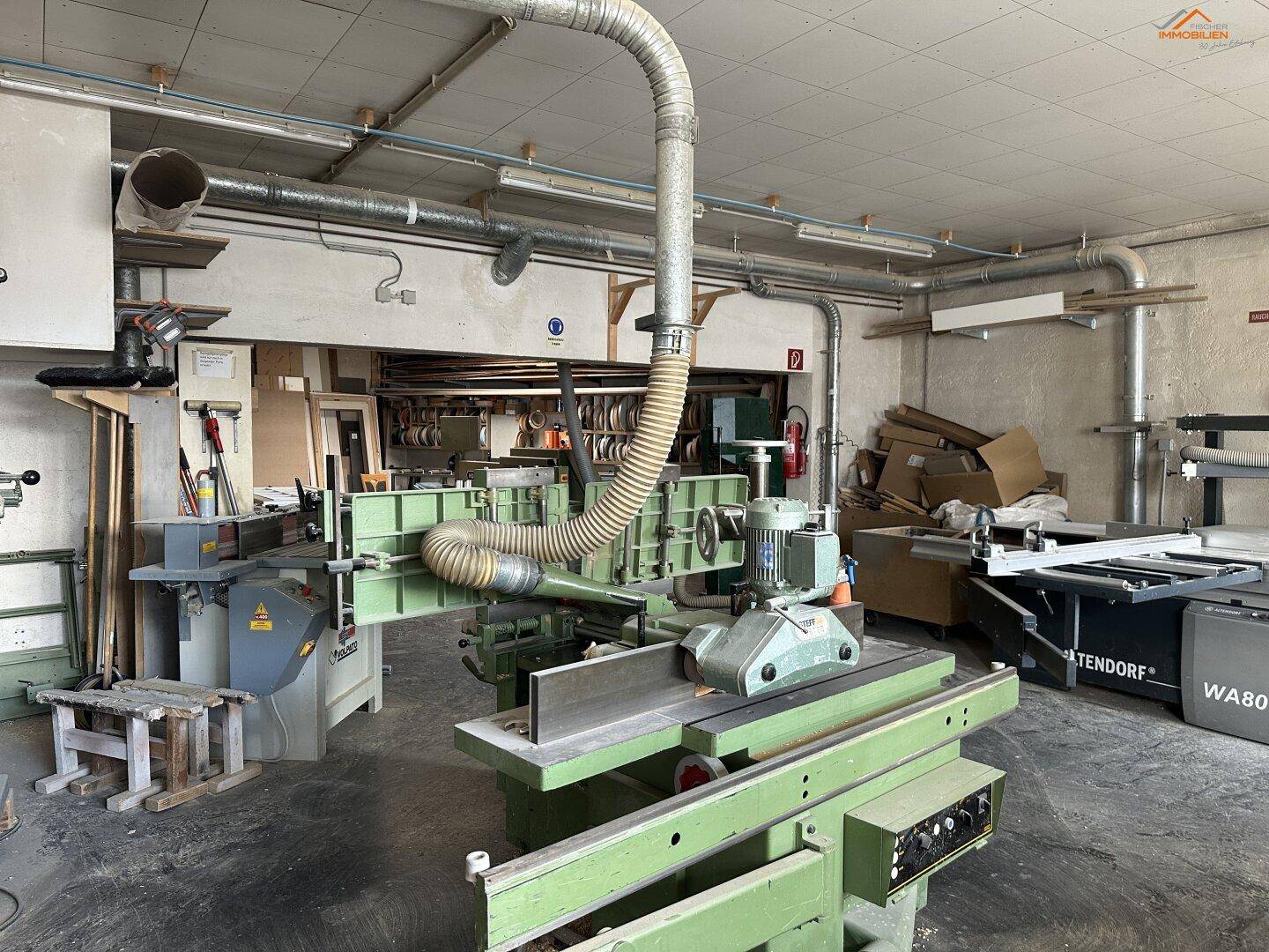 Detailansicht einer großen grünen Holzbearbeitungsmaschine mit Absauganlage in einer belebten Werkstatt.