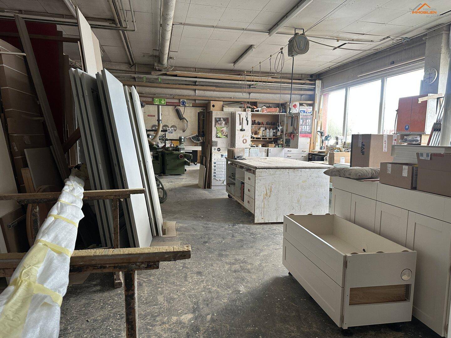 Geräumige Holzwerkstatt mit mehreren Arbeitsbereichen, Materiallager und großen Fenstern für viel Helligkeit.