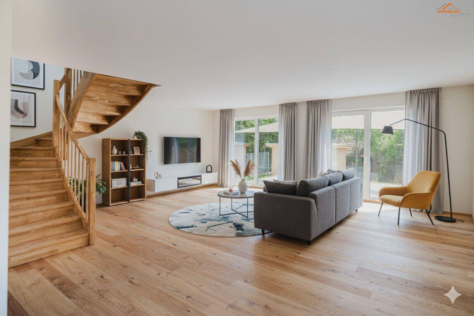 Geräumiges Wohnzimmer mit heller Holzboden, moderner Einrichtung und großer Holztreppe zum Obergeschoss.