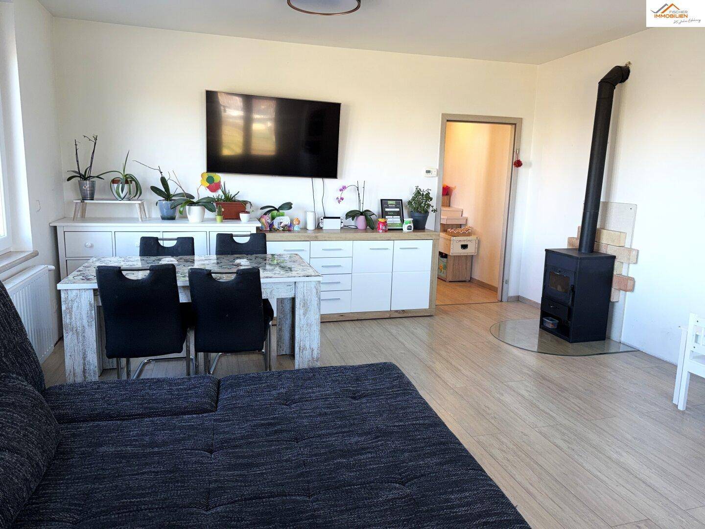 Gemütlicher Wohnbereich mit Holzofen, Esstisch und Fernseher an der Wand.