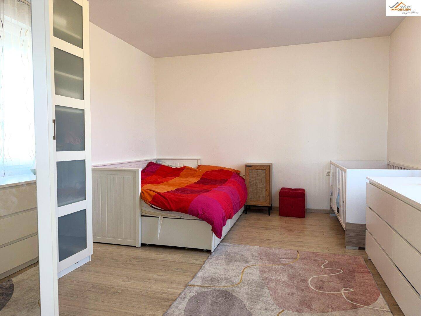 Schlafzimmer mit hellem Laminatboden, Kinderbett und einem Kleiderschrank.