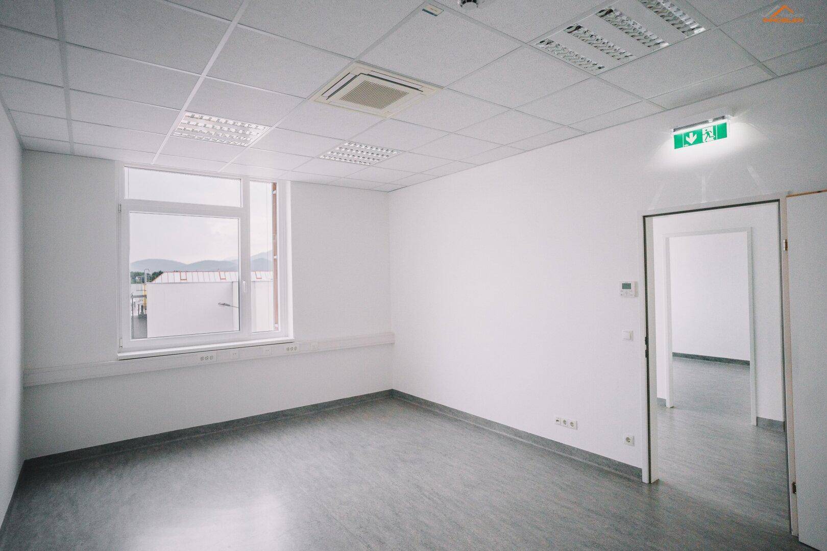 Geräumiger, leerer Büroraum mit großen Fenstern und viel Tageslicht.