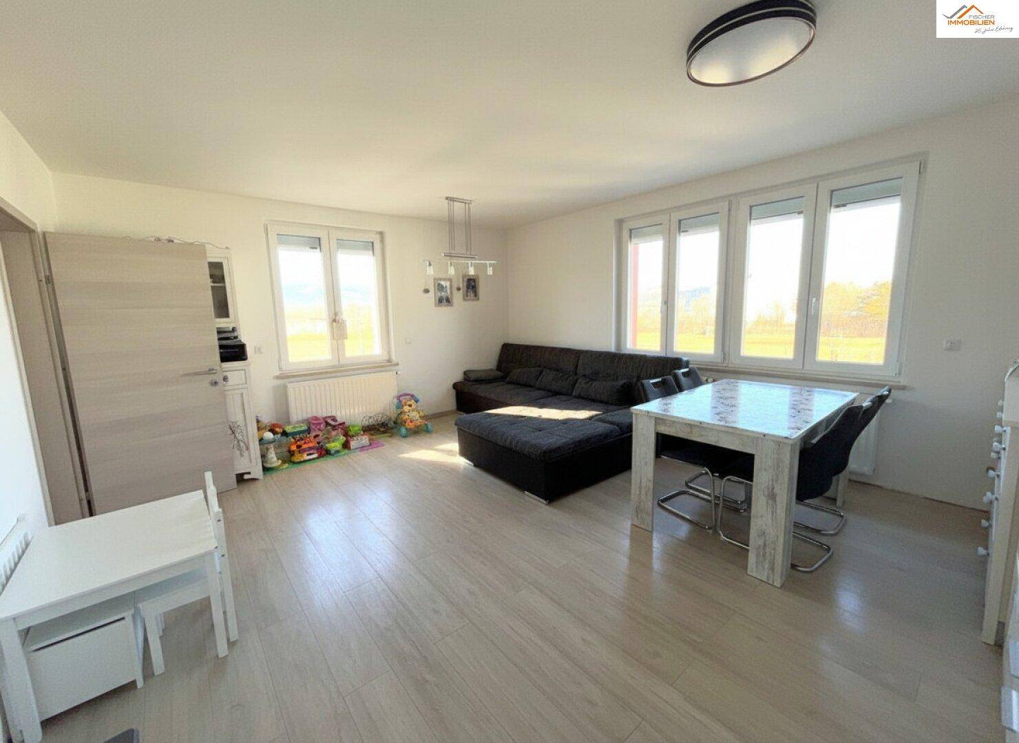 Helles Wohn-Esszimmer mit Laminatboden, großzügigen Fenstern und modernem Mobiliar.