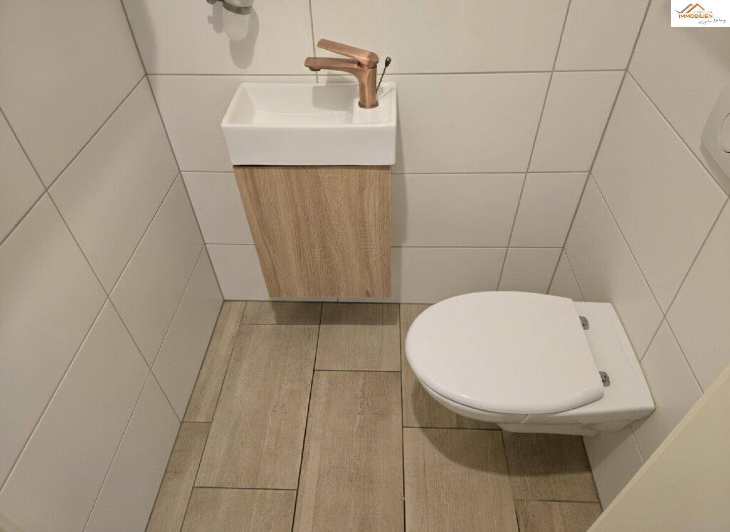 Kleines Gäste-WC mit wandhängender Toilette und modernem Waschbecken, gefliest in Weiß und Holzoptik.