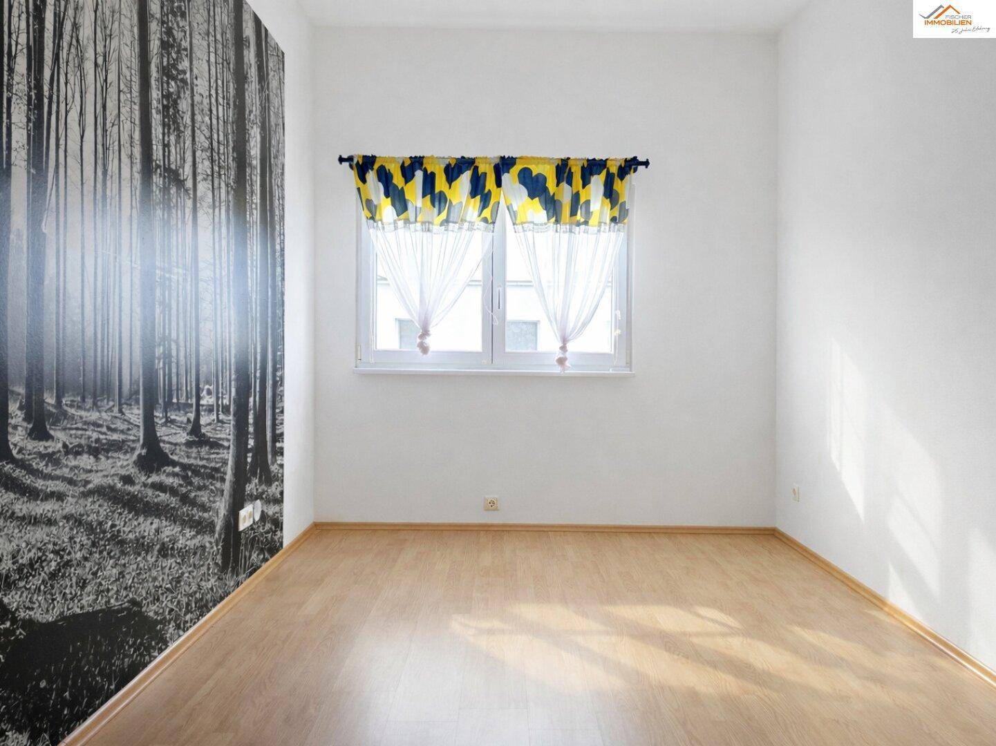 Heller Raum mit Laminatboden und einer Akzentwand mit Waldmotiv-Tapete, ideal für individuelle Gestaltung.