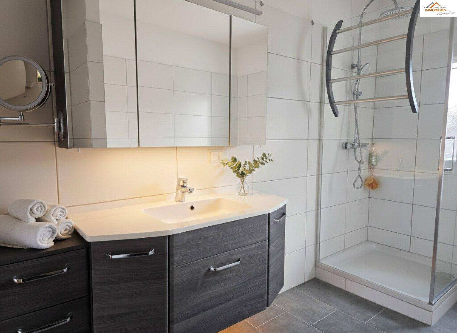 Modernes Badezimmer mit Waschtisch, Spiegelschrank und Duschkabine, ausgestattet mit Handtuchhalter.