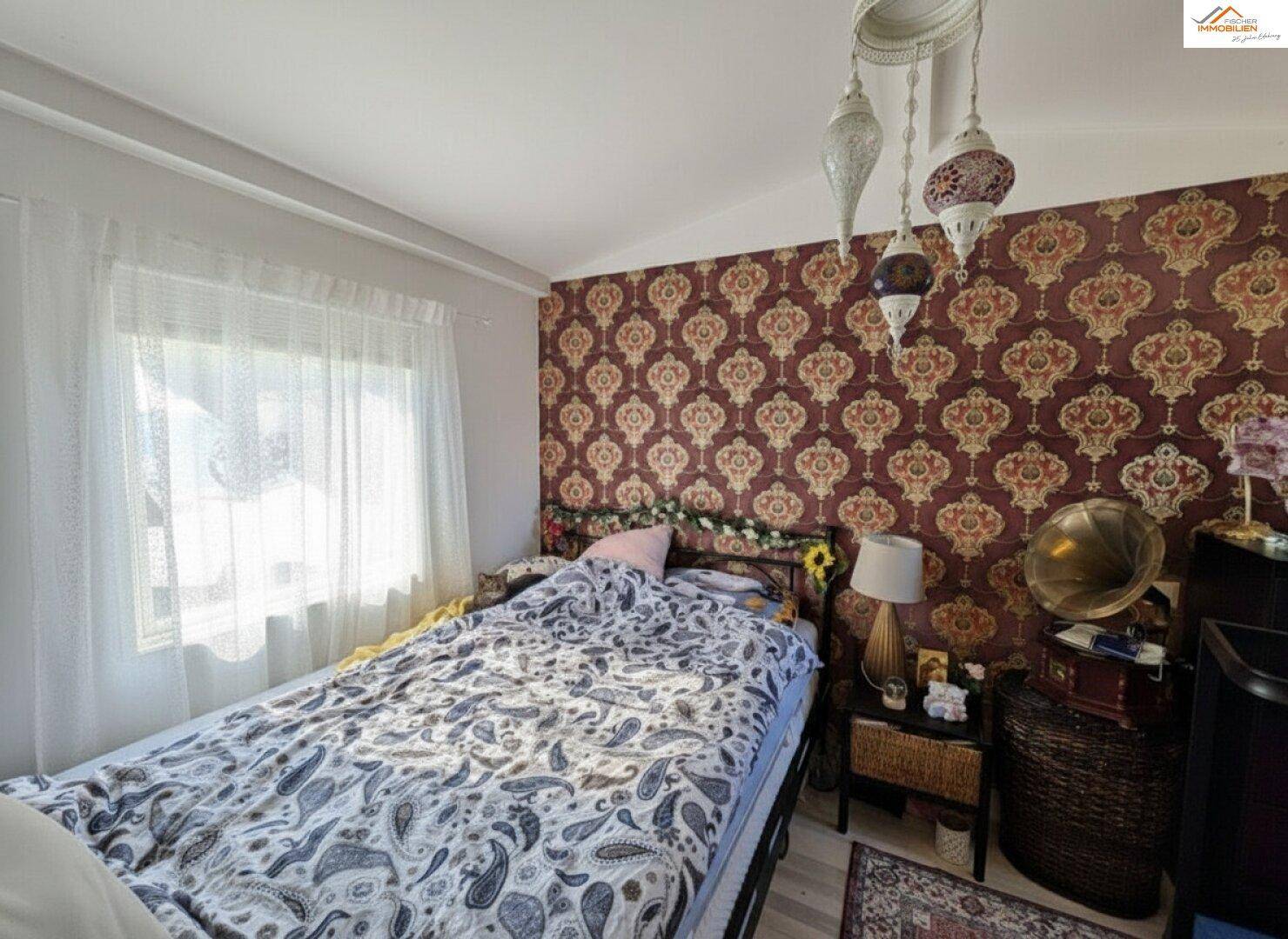 Schlafzimmer mit gemusterter Tapete, großem Bett und dekorativen Hängelampen.