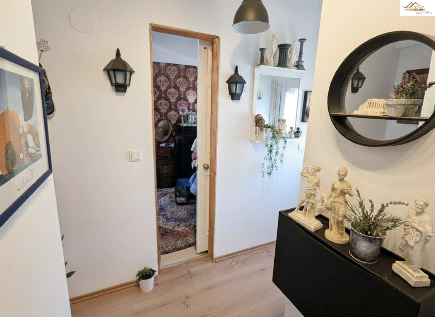 Flur mit Holzboden und Blick in ein angrenzendes Zimmer mit gemusterter Tapete.
