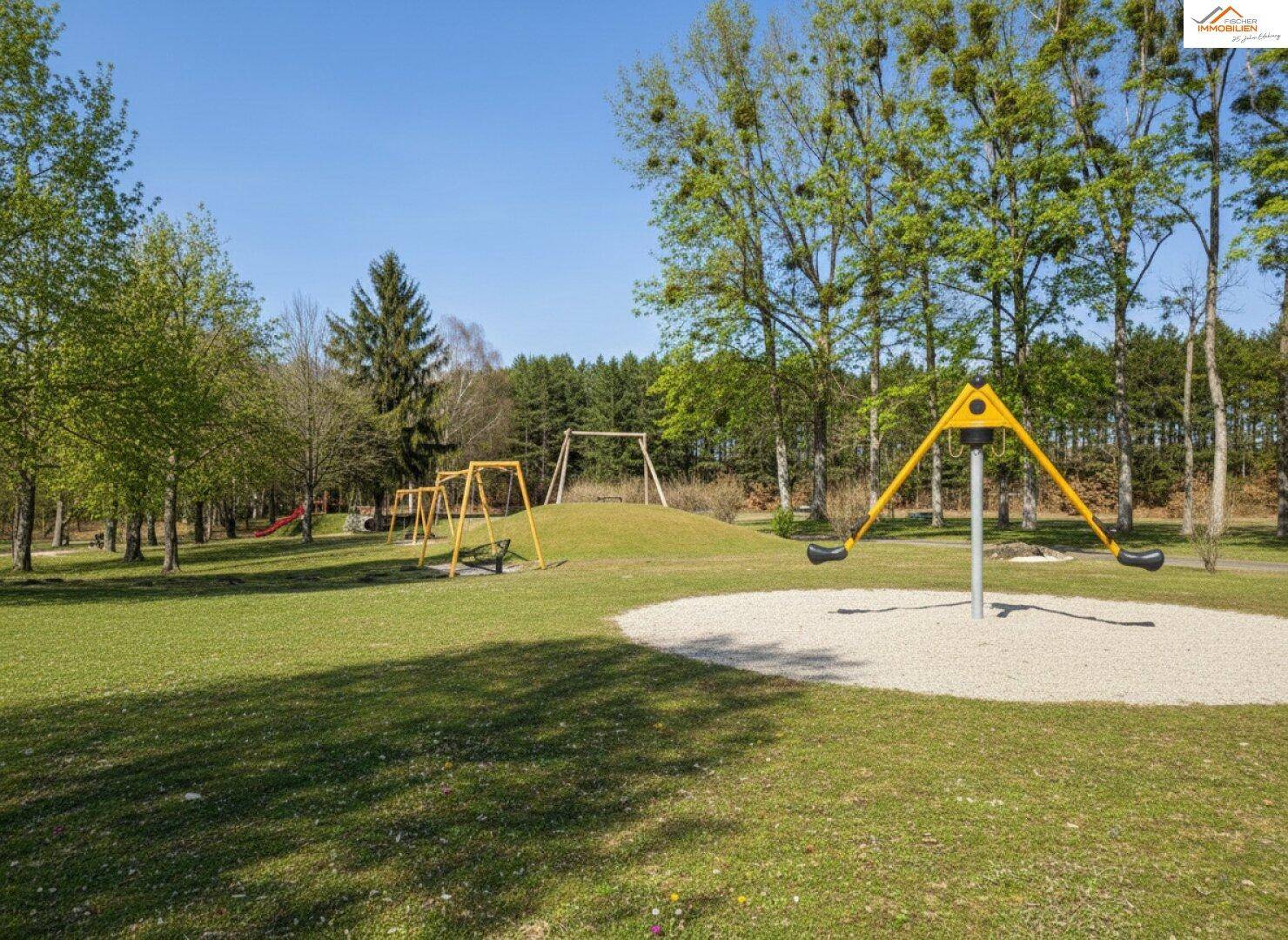 Großer Spielplatz mit Schaukeln und Wippen in einer grünen Parkanlage.