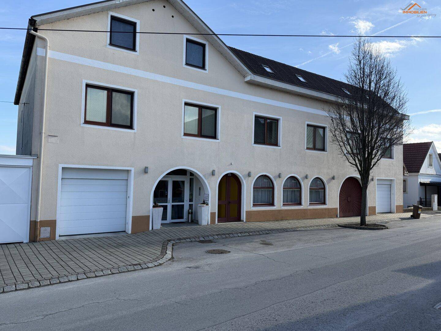 Ansicht des Gebäudes von der Straße mit Garagen und einem Baum im Vordergrund.