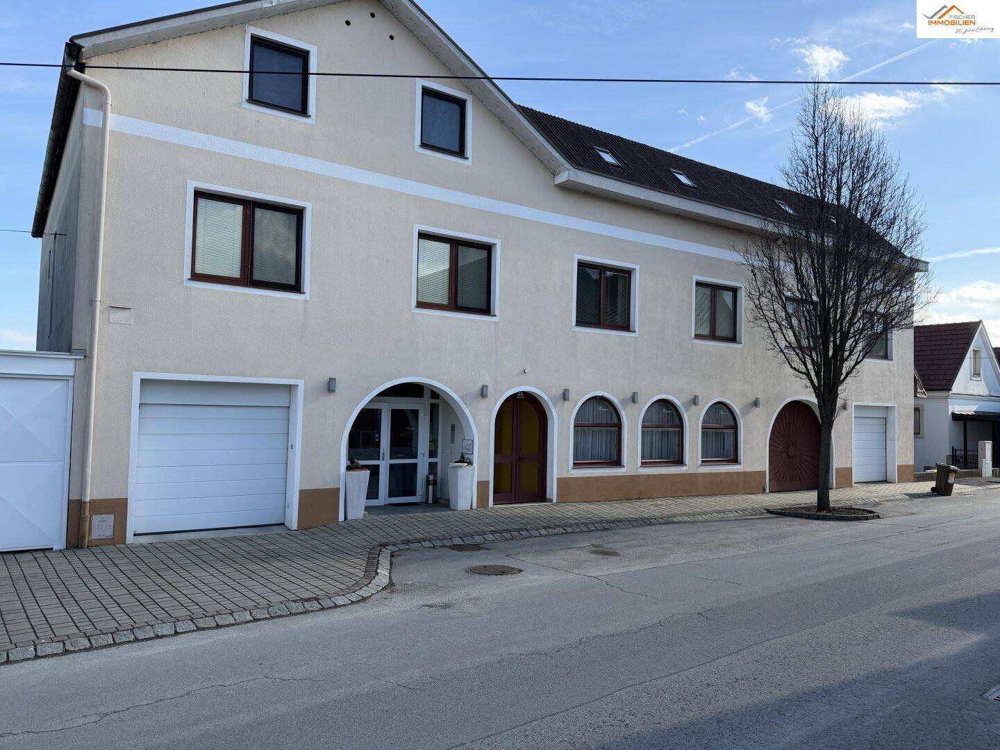 Gebäudeansicht mit Garagen, Eingangsbereich und Fenstern, die auf die Straße blicken.