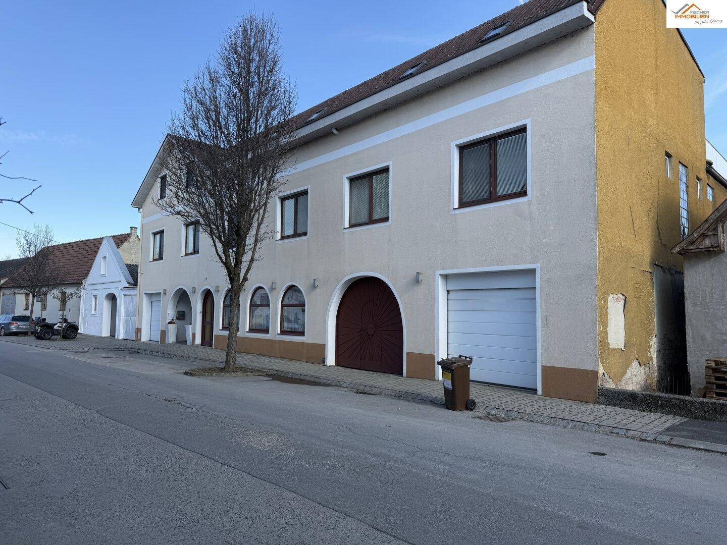 Seitenansicht des Gebäudes mit Garagentor und angrenzendem gelbem Anbau unter blauem Himmel.