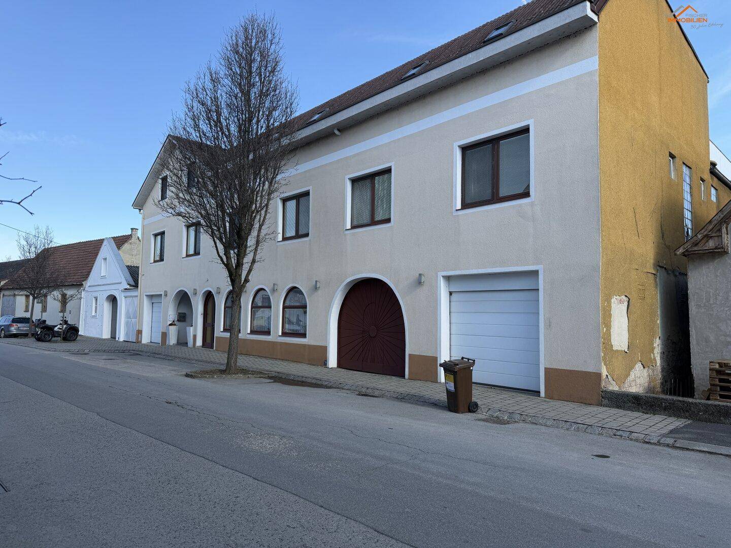 Seitenansicht des Gebäudes mit Garagentor und angrenzenden älteren Häusern.