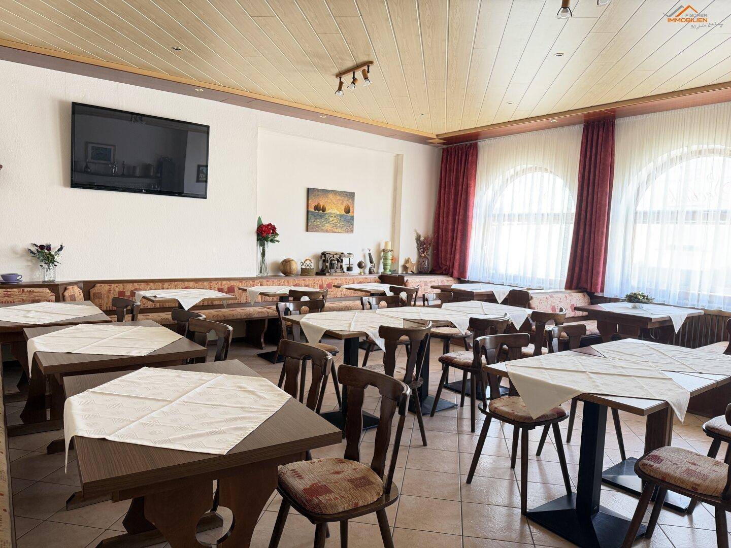 Geräumiger Speisesaal mit vielen Tischen, Stühlen und traditioneller Holzdecke.