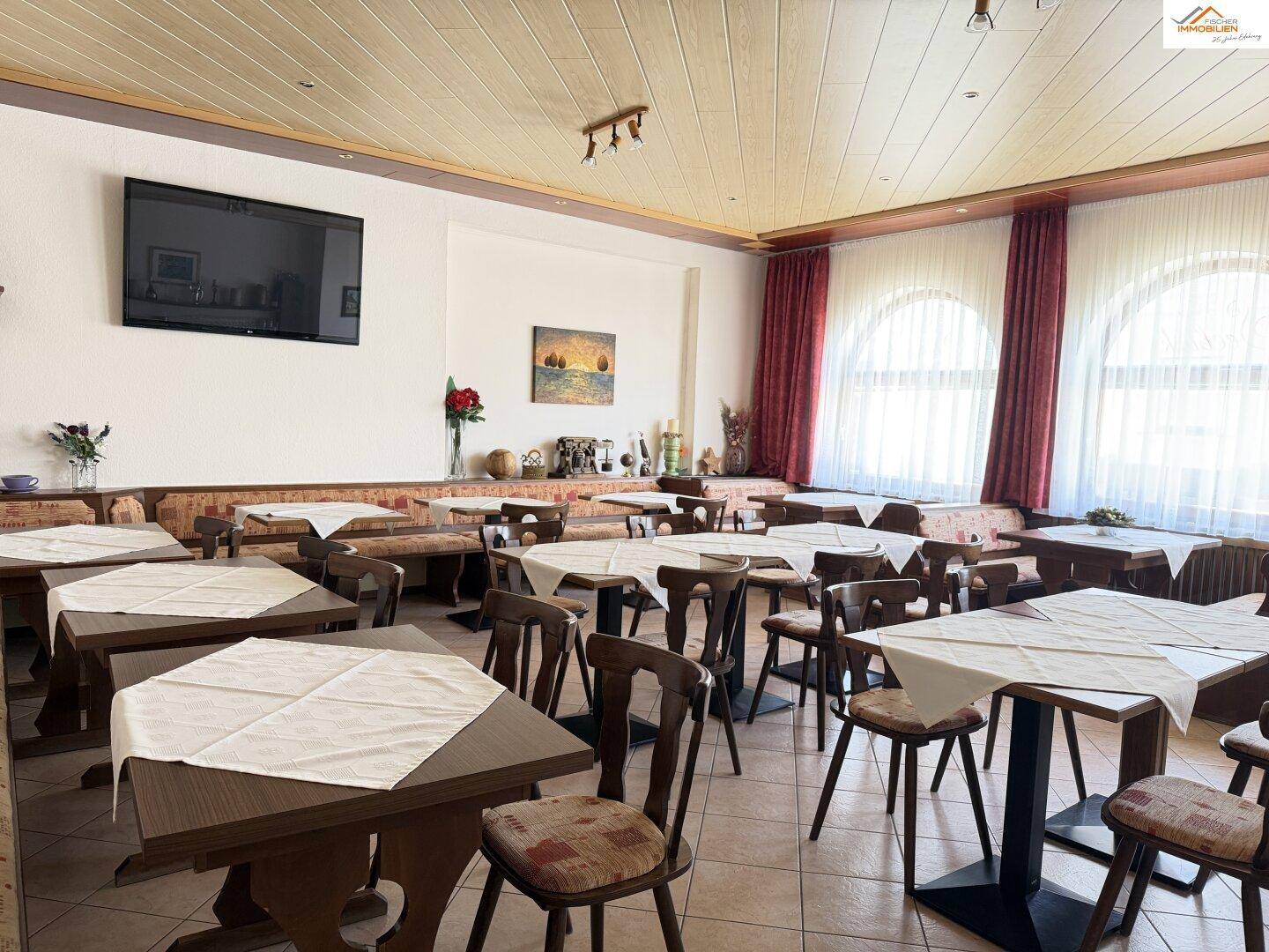 Geräumiger Speisesaal mit vielen Tischen, Stühlen und großen Rundbogenfenstern.