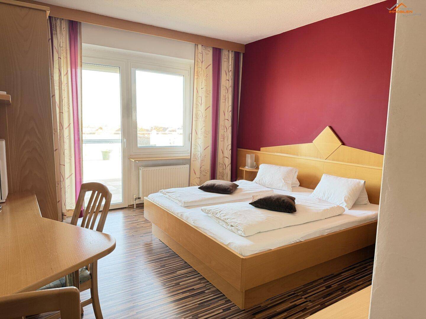 Helles Schlafzimmer mit Doppelbett, Holzboden und Zugang zu einem Balkon.