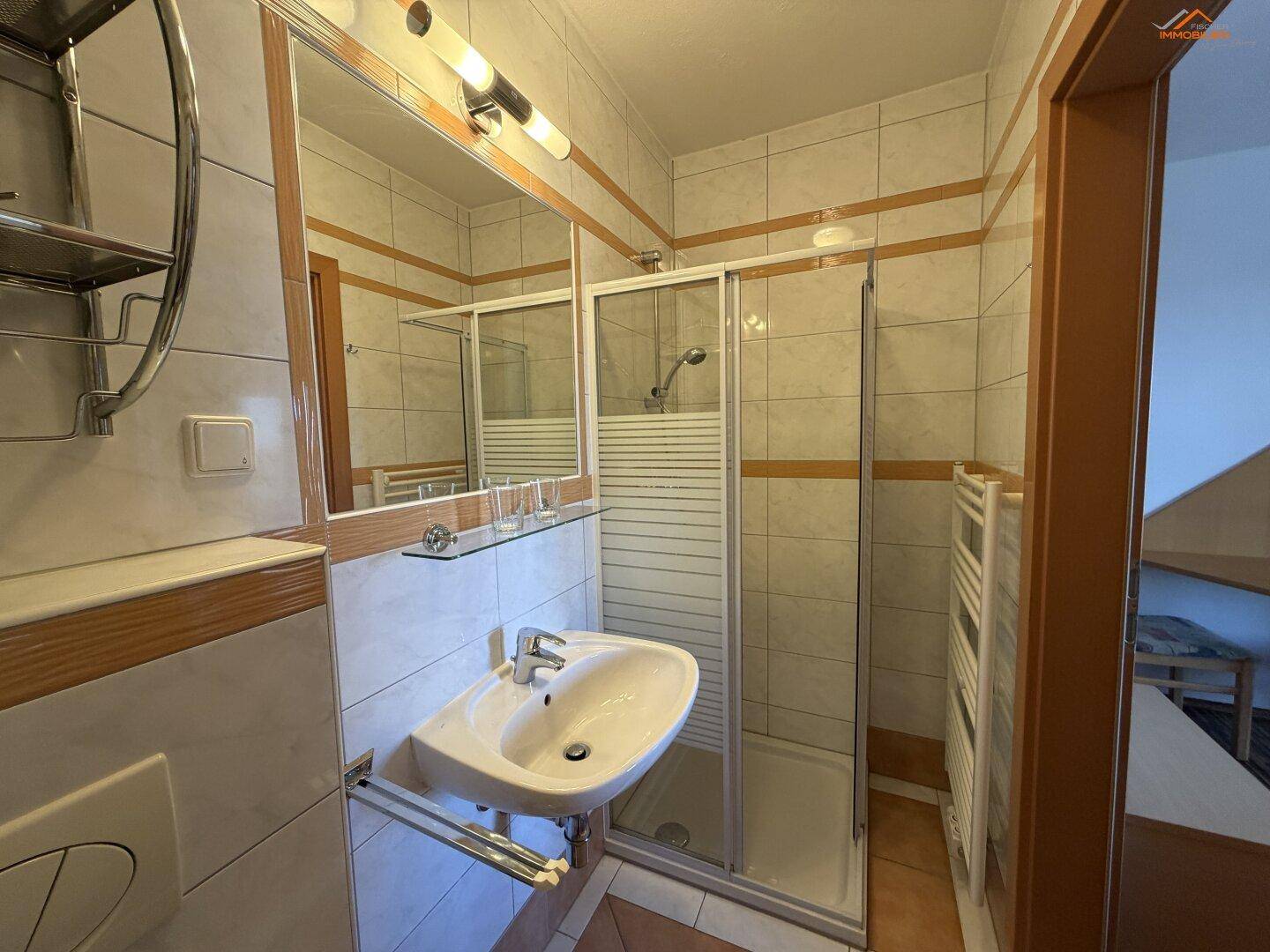 Modernes Badezimmer mit Dusche, Waschbecken und hellen Fliesen.