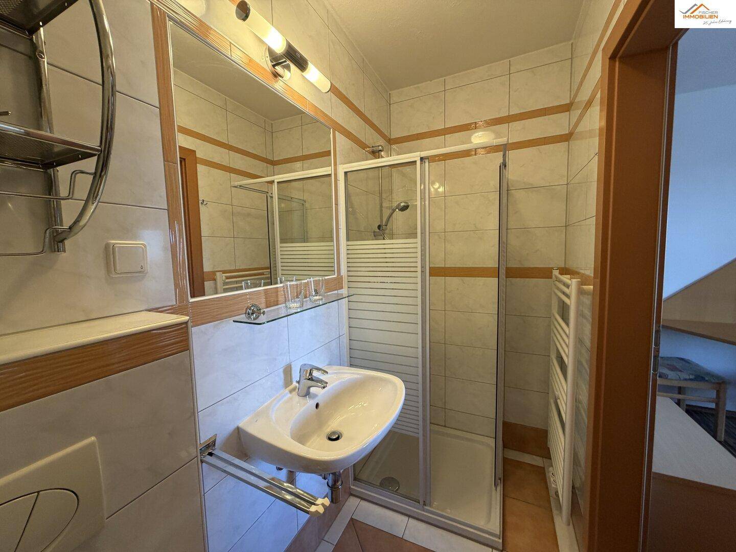Helles Badezimmer mit Dusche, Waschbecken und Wand-WC in neutralen Fliesen.