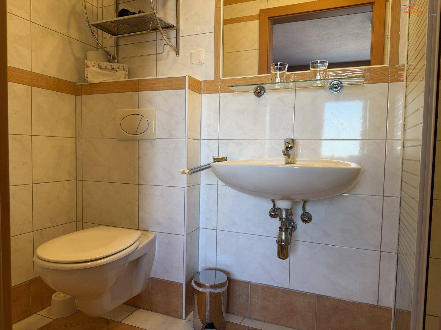 Funktionales Badezimmer mit WC, Waschbecken und gefliesten Wänden in neutralen Farben.