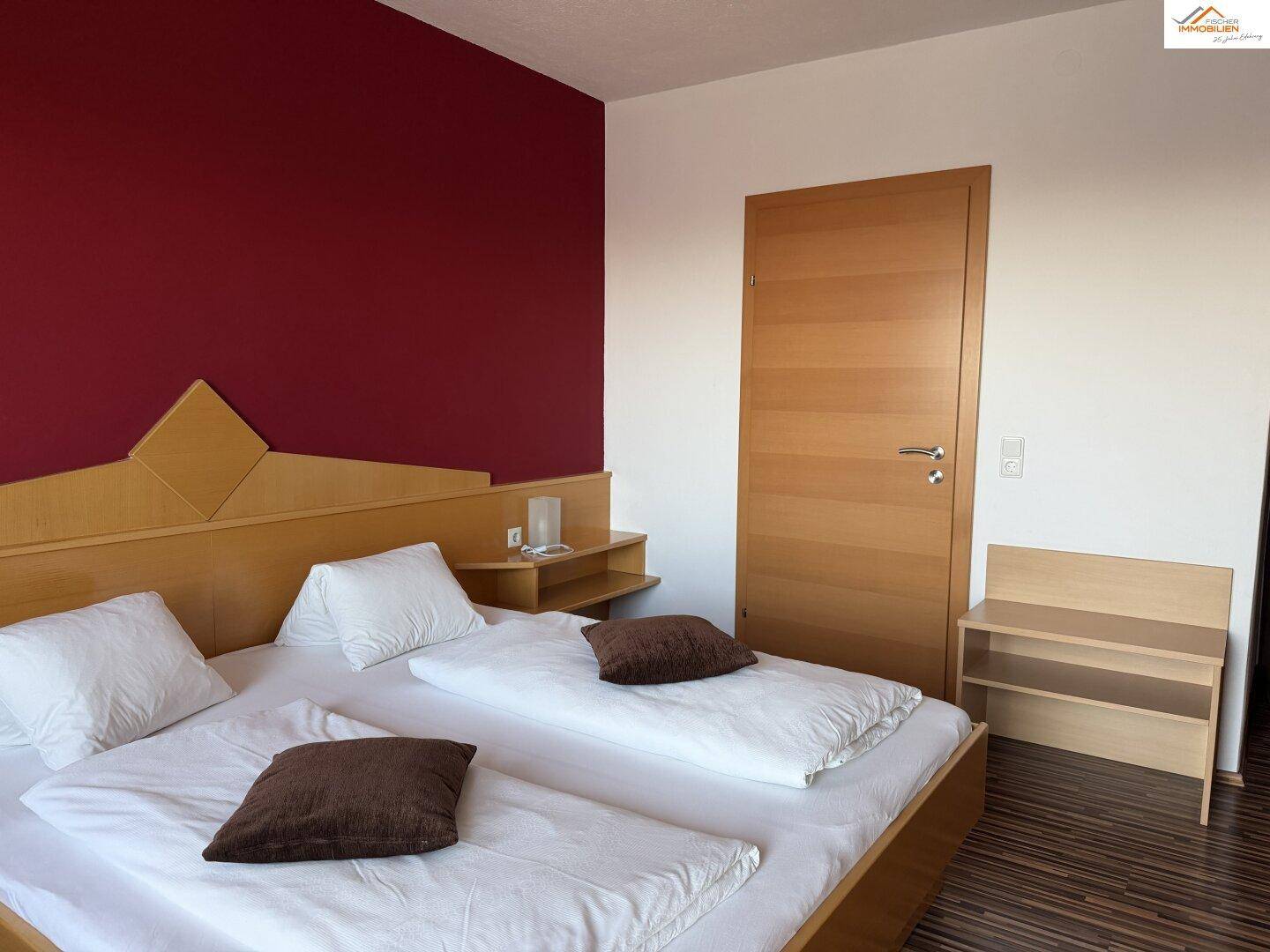 Schlafzimmer mit Doppelbett, Holzboden und Holztür, in warmen Farben gestaltet.