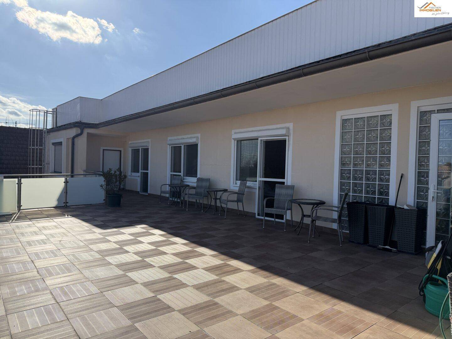 Große Dachterrasse mit Fliesenboden und Sitzgelegenheiten unter blauem Himmel.