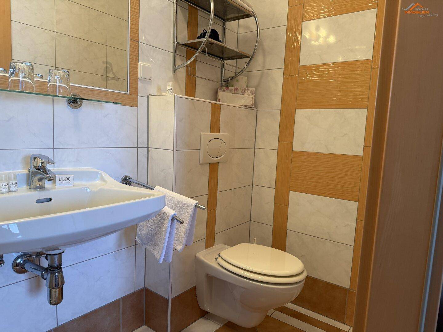 Badezimmer mit WC, Waschbecken und hellen Fliesen in verschiedenen Mustern.