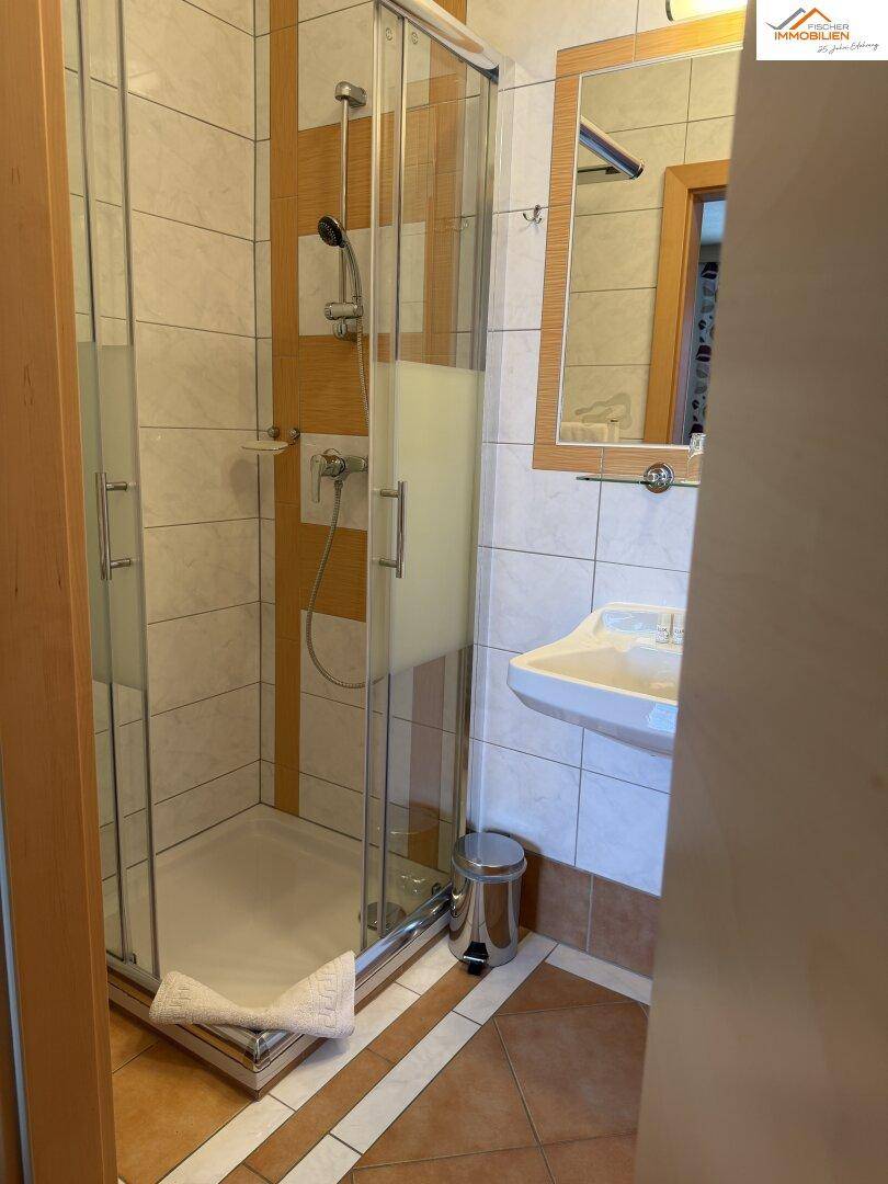 Badezimmer mit Duschkabine, Waschbecken und Spiegel in neutralen Fliesen.