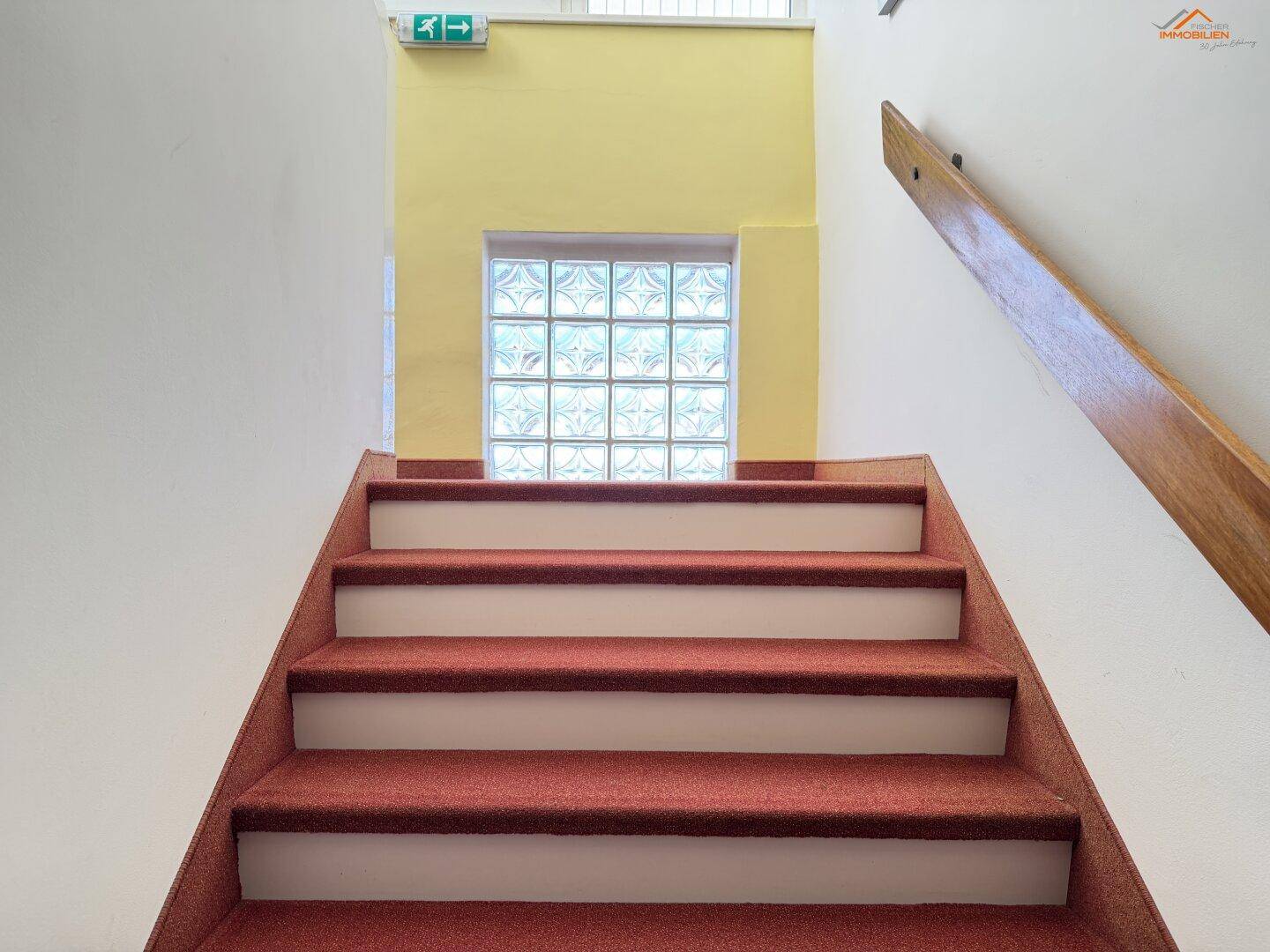 Treppenhaus mit rotem Teppichboden, gelber Akzentwand und Glasbausteinfenster für natürliches Licht.