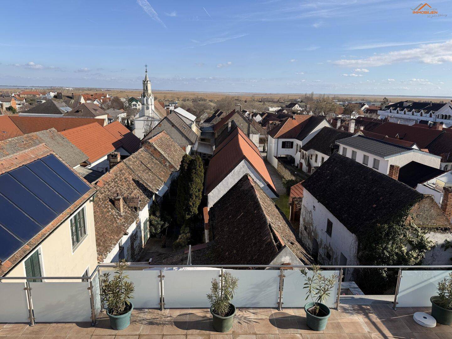 Dachterrasse mit weitem Blick über ein Dorf mit roten Dächern und einer Kirche im Hintergrund.