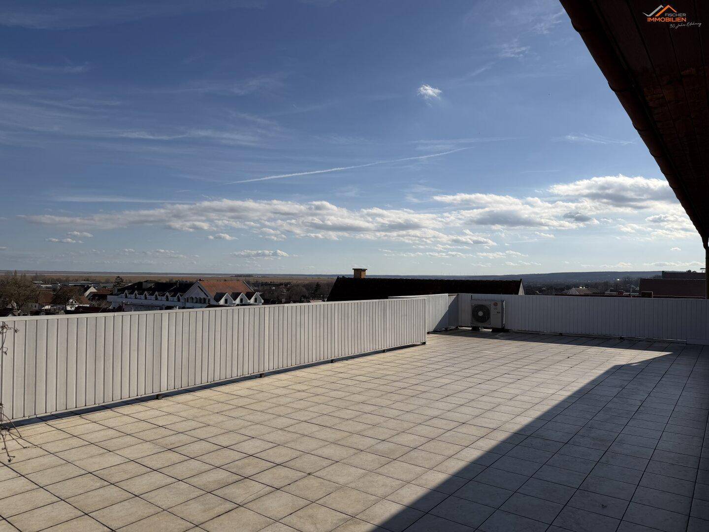 Geräumige, geflieste Dachterrasse mit weißer Brüstung und weitem Blick über die Umgebung.