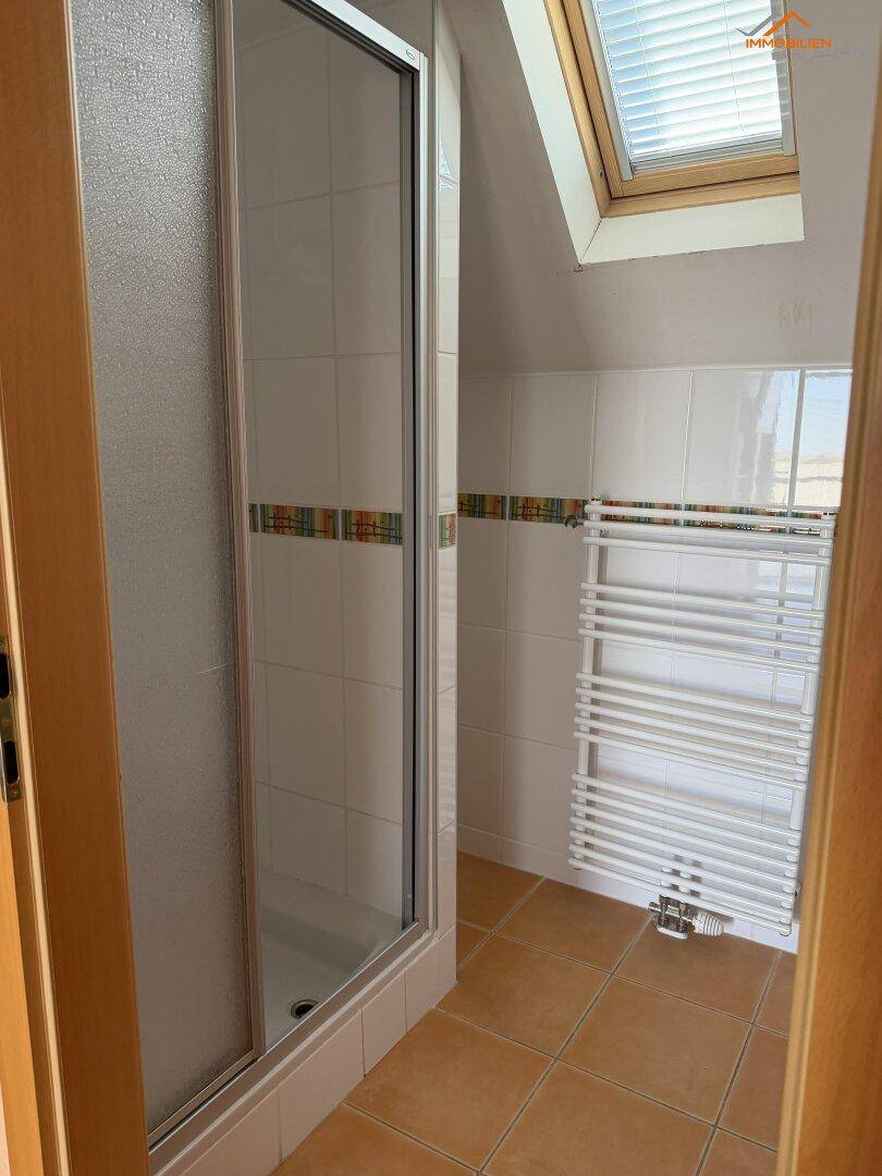 Badezimmer mit Duschkabine, Fliesenboden, beheiztem Handtuchhalter und Dachfenster.
