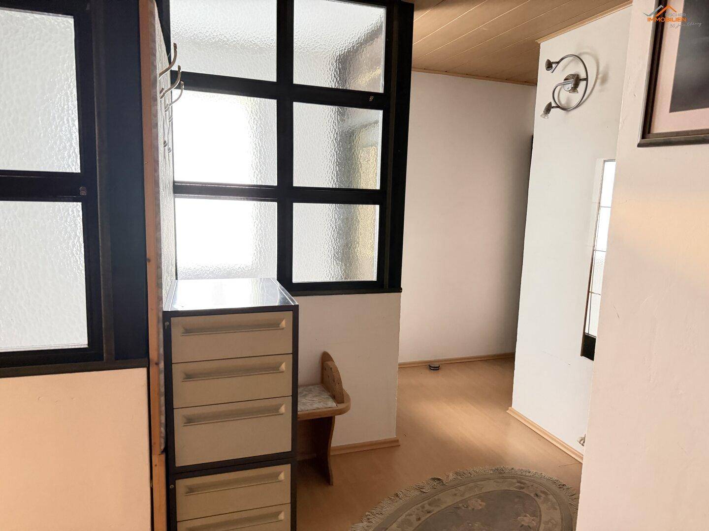 Heller Eingangsbereich mit Holzboden, kleinem Schrank und Fenster mit Sprossen.