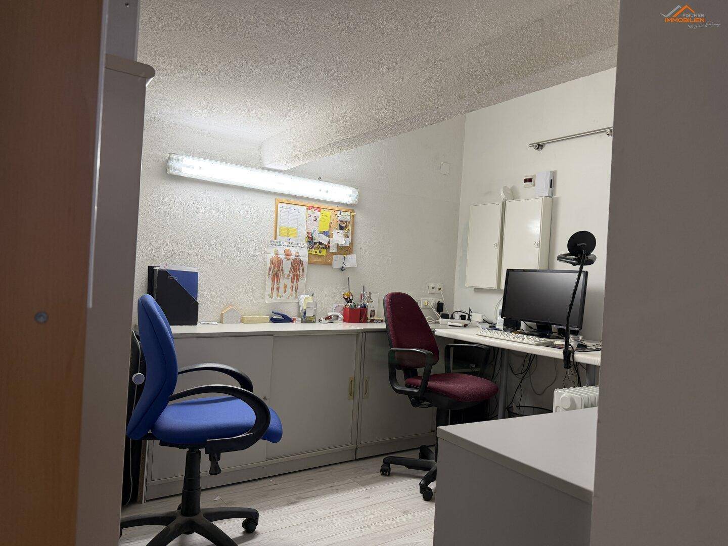 Funktionales Büro mit zwei Bürostühlen, Schreibtisch und einer Pinnwand.