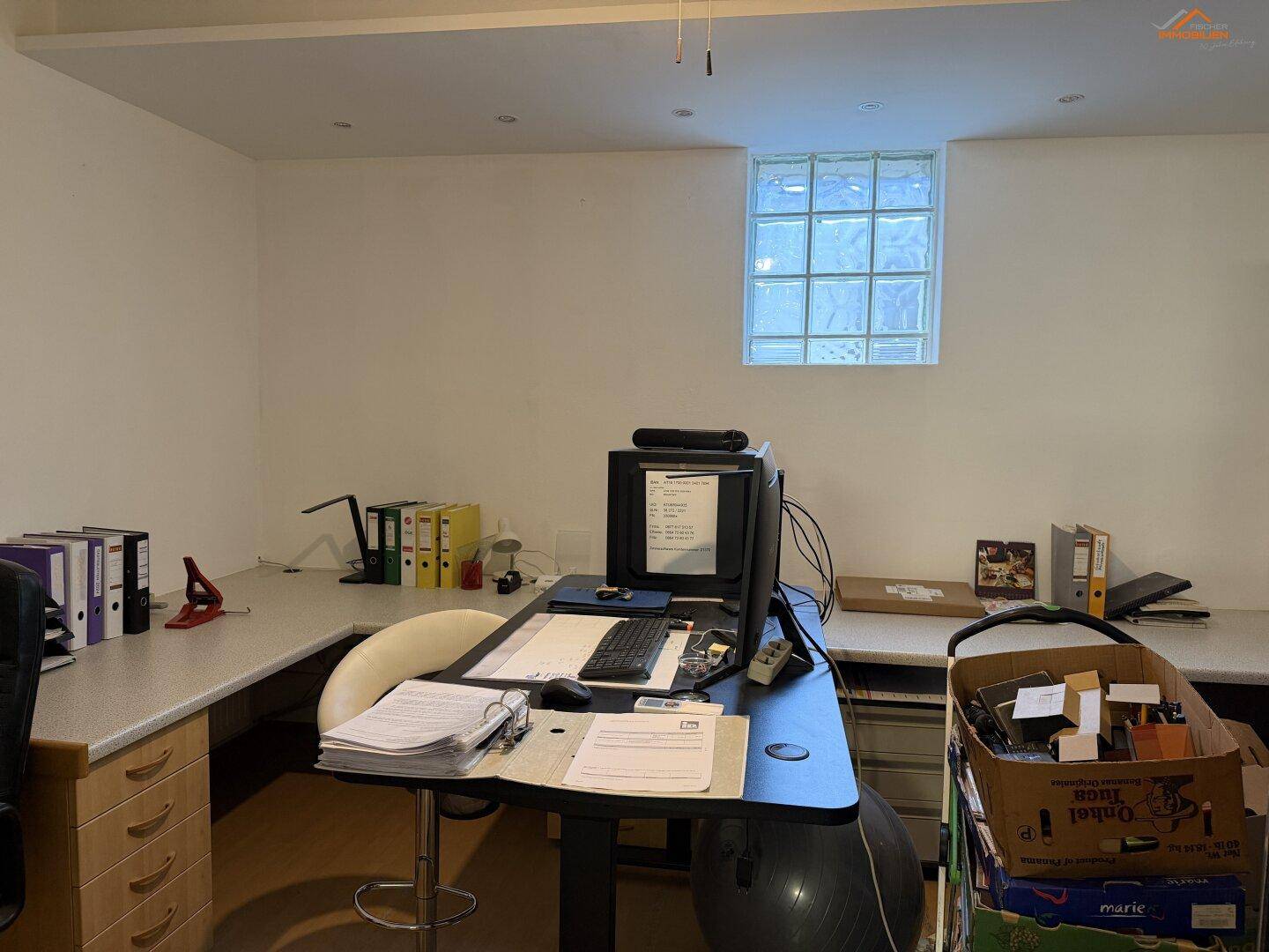 Geräumiges Büro mit mehreren Schreibtischen, Bürostühlen und einem Glasbausteinfenster.