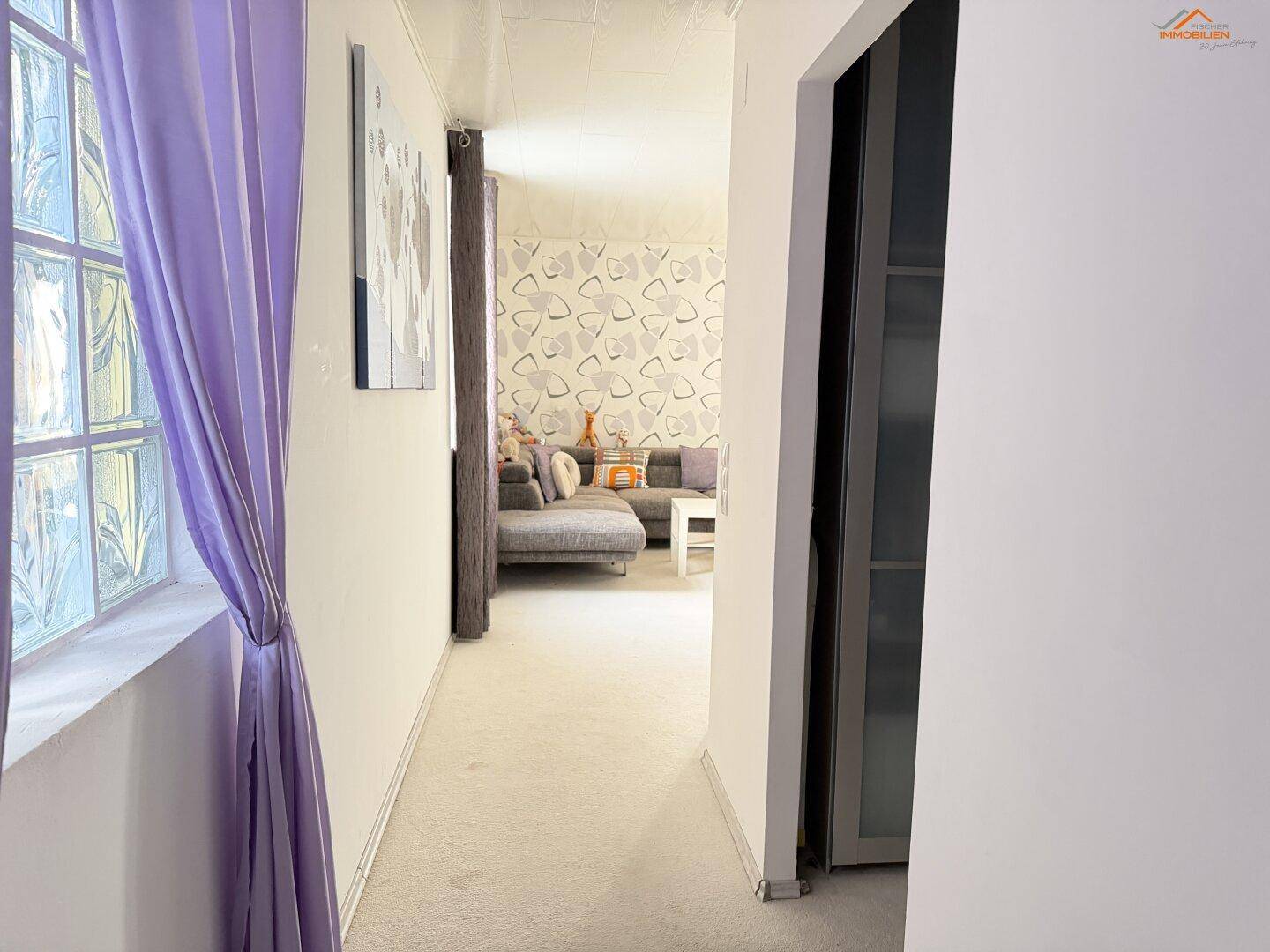 Flur mit lila Vorhang, Glasbausteinfenster und Blick in ein angrenzendes Wohnzimmer.