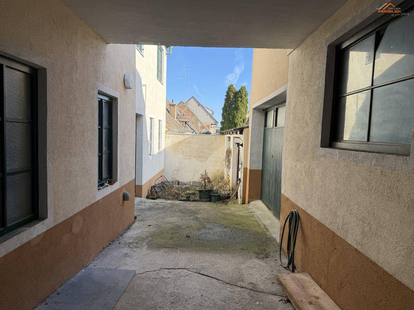 Schmaler Außenbereich zwischen Gebäuden mit Betonboden und Blick zum Himmel.