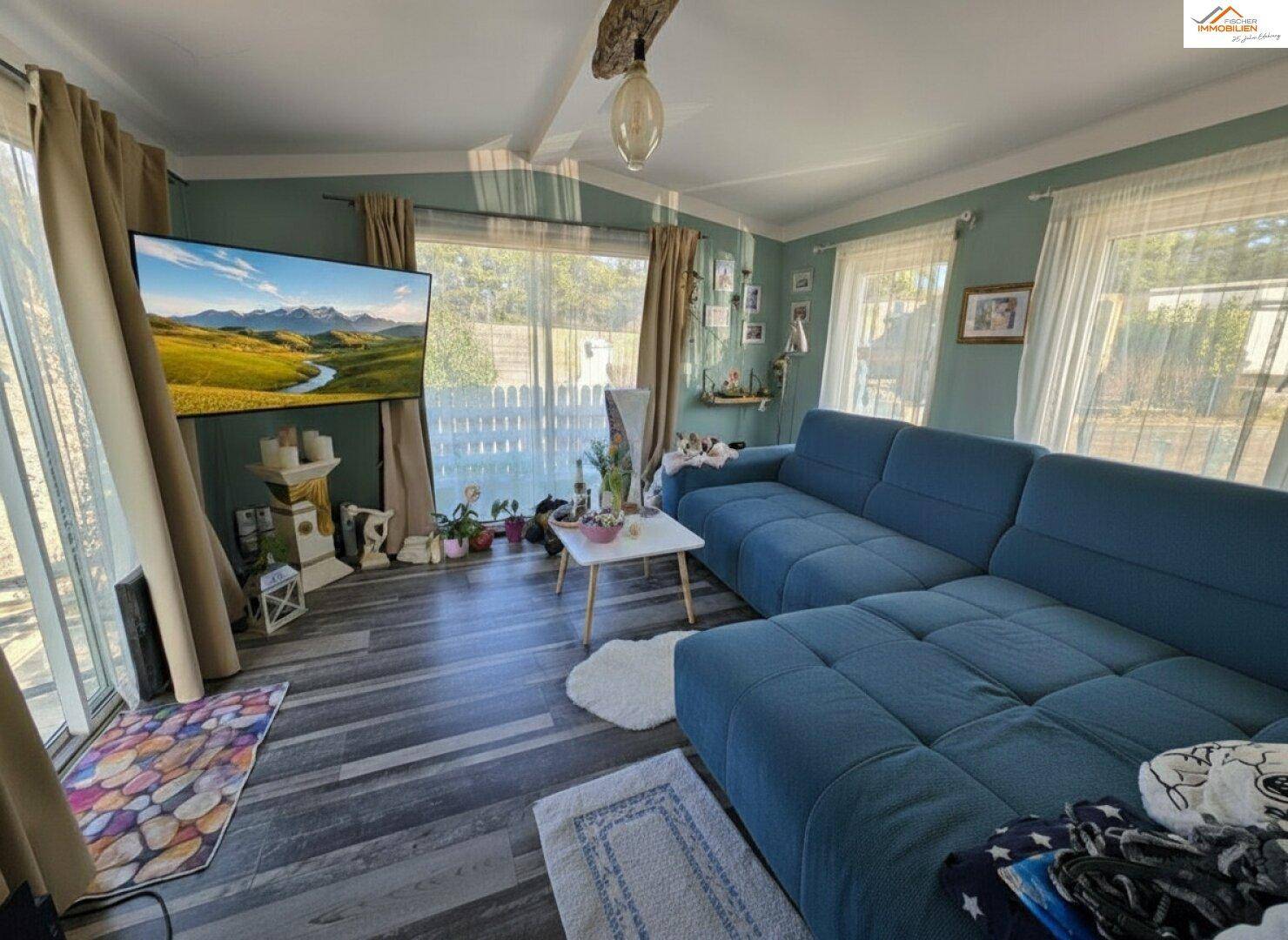 Geräumiges Wohnzimmer mit großem blauen Sofa, Holzbalken und vielen Fenstern.