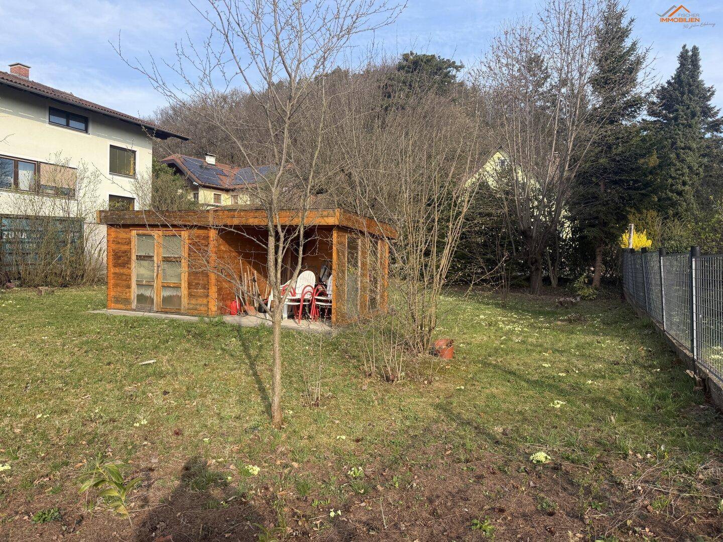Gartenbereich mit einem Holzschuppen, der Gartenmöbel beherbergt, und einem Zaun im Vordergrund.