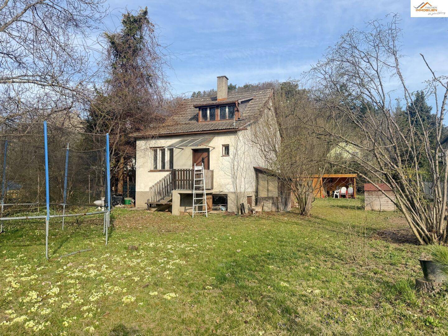 Ansicht des Hauses vom Garten aus mit Trampolin und einem weiteren Holzschuppen im Hintergrund.