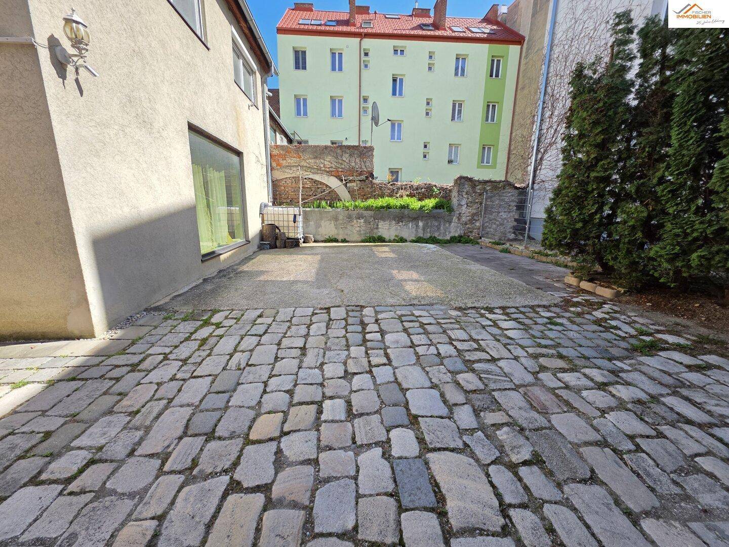 Offener Hinterhofbereich mit Kopfsteinpflaster und einer angrenzenden Mauer mit Bewuchs.
