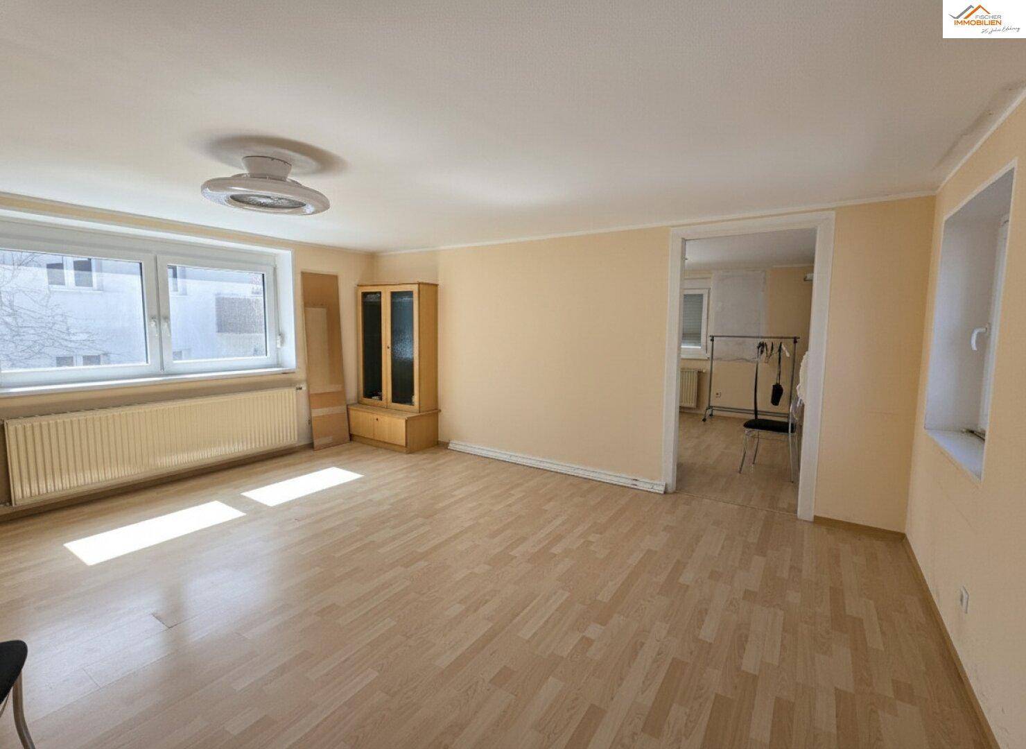 Geräumiges Wohnzimmer mit Laminatboden, großen Fenstern und viel natürlichem Licht.